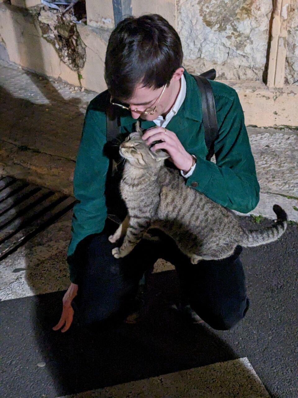 Me squatting in the streets of Pollença, Mallorca with a tabby cat which climbed on my legs and is enjoying the pets.